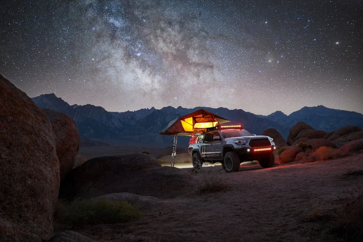 Truck with a lit rooftop tent under the Milky Way